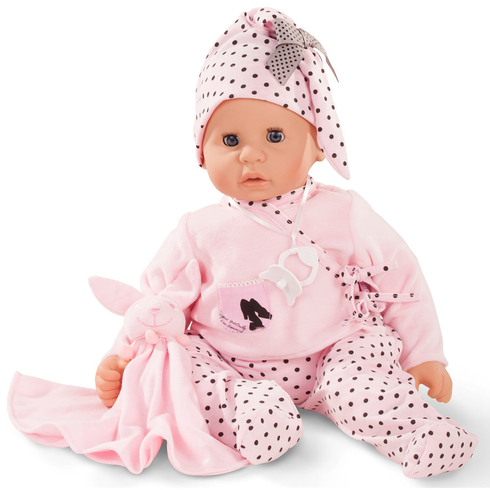 Baby doll with blue sleeping eyes wearing pink polka-dot bonnet, pink cardigan, and polka-dot pants, holding a pink plush toy