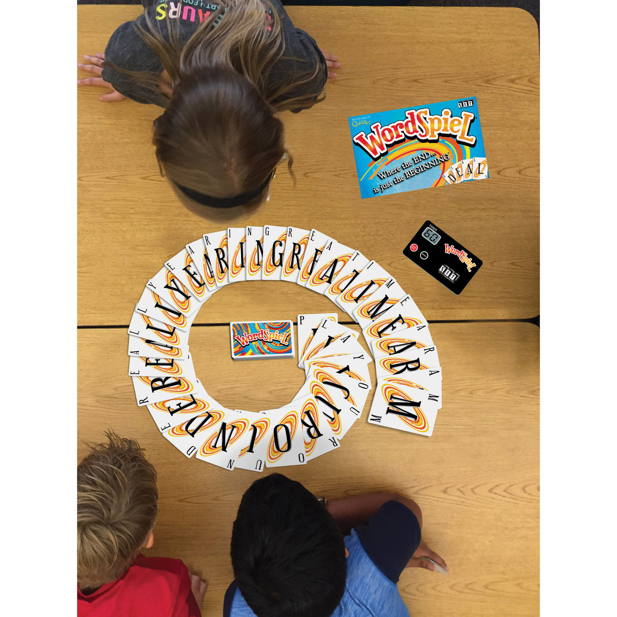 WordSpiel card game displayed in spiral layout on wooden table with players and game box visible