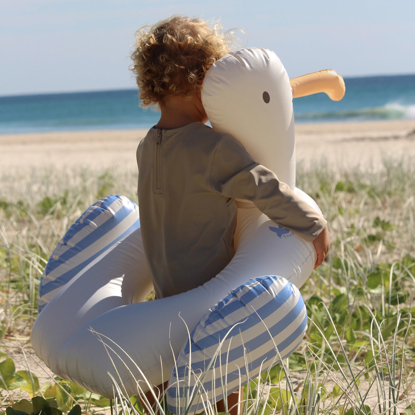 Sammy the Seagull pool float ring in blue and white stripes, held by child at beach