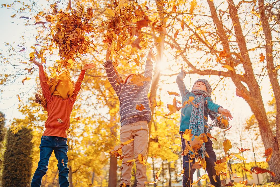 Kids tossing leaves in the air outside on a fall day