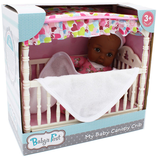 Baby doll with brown skin in white canopy crib with pink and white patterned bedding, blanket, and pillow