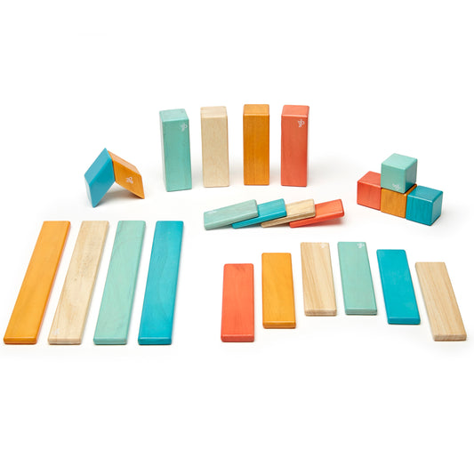 Tegu 24-piece magnetic wooden block set in sunset colors including turquoise, natural wood, orange, and coral in various rectangular and cube shapes arranged on