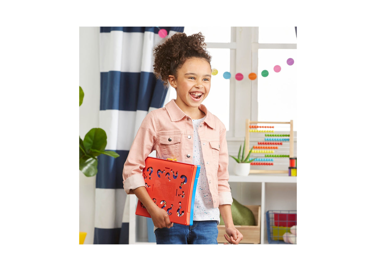 Child holding red Hasbro Guess Who Classic Character Guessing Game with blue accents in colorful playroom