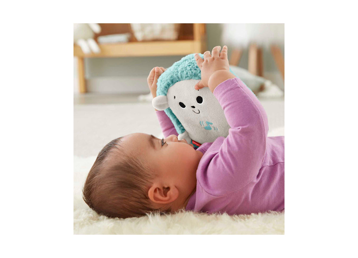 Fisher-Price Calming Vibes Hedgehog Soother plush toy with turquoise and white body held by baby in pink outfit