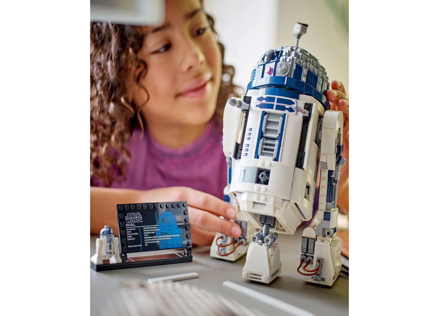 Girl holding LEGO Star Wars R2-D2 buildable figure with blue and white details and instruction manual
