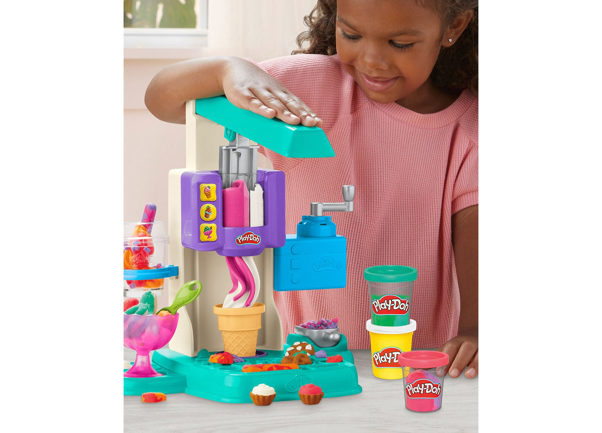 Child in pink shirt using Play-Doh Rainbow Swirl Ice Cream Playset with turquoise machine, purple mixer, blue contain...