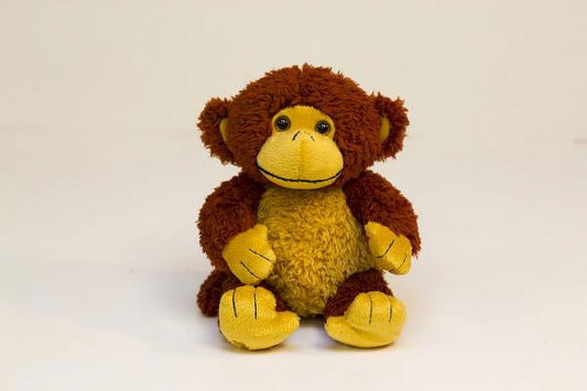 Brown and yellow plush monkey with embroidered smile, sitting upright on plain background