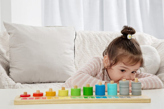 Child on model playing with colorful wooden ring stacker toy on white surface, with stacked rings in rainbow order