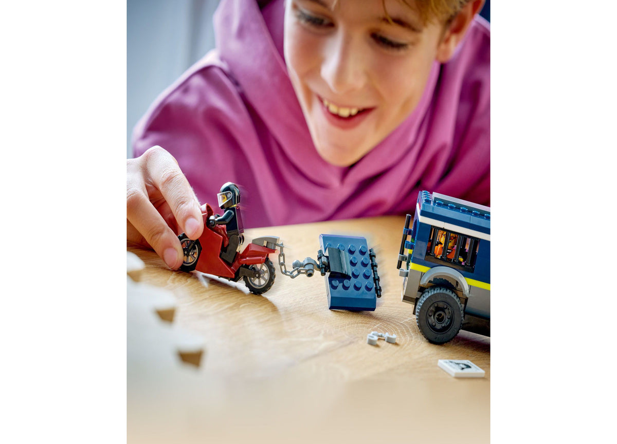Child in purple shirt playing with LEGO City Police Prisoner Transport Van set, featuring blue van, red motorcycle, a...