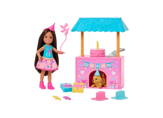 Barbie Club Chelsea doll with long brown hair wearing pink party hat and blue top, holding magic wand, standing next to pink birthday party kiosk with blue awni