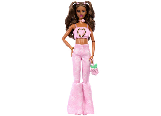 Barbie doll with brown hair in pigtails wearing pink heart crop top, pink patterned flare pants, and holding a small pink rose bag