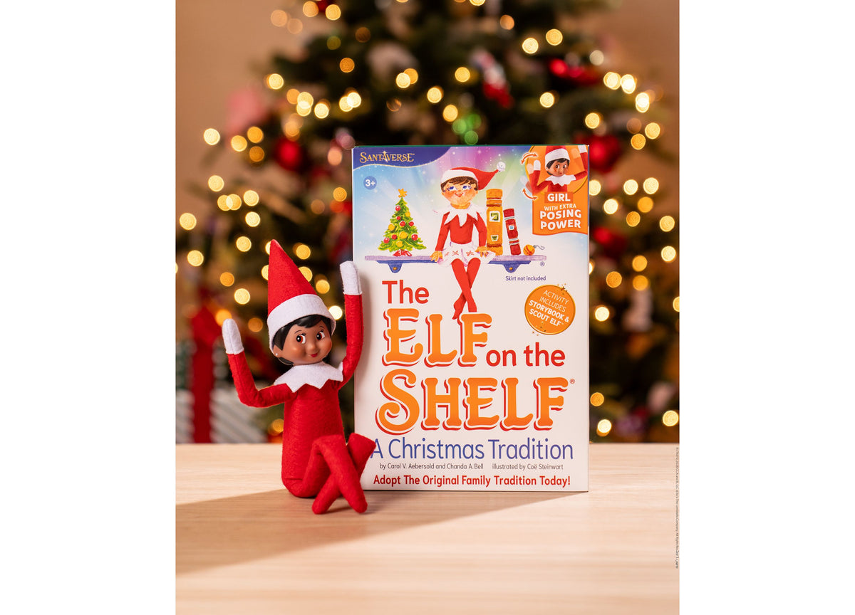 Elf on the Shelf Scout Elf Girl figure with poseable limbs next to storybook box against decorated Christmas tree