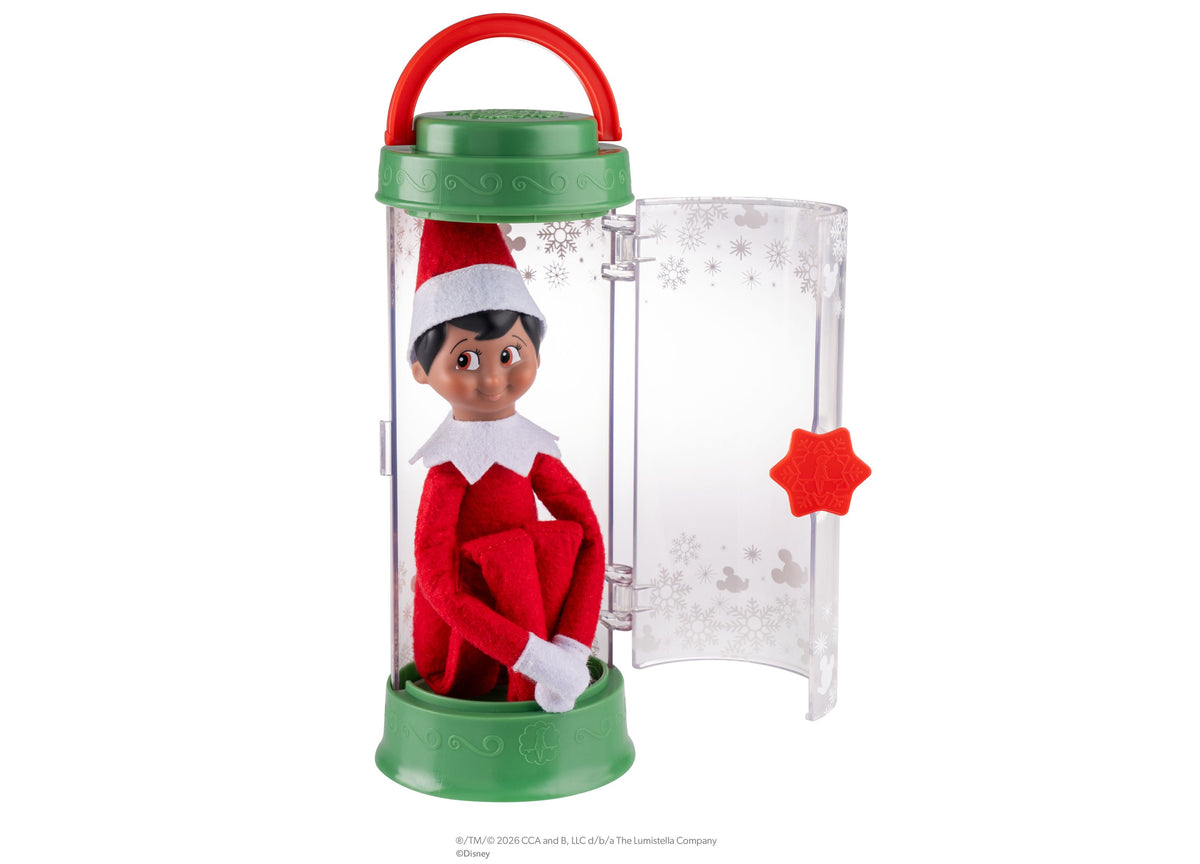 Elf on the Shelf Scout Elf in red and white outfit with Santa hat inside green and clear carrier with red star sticker