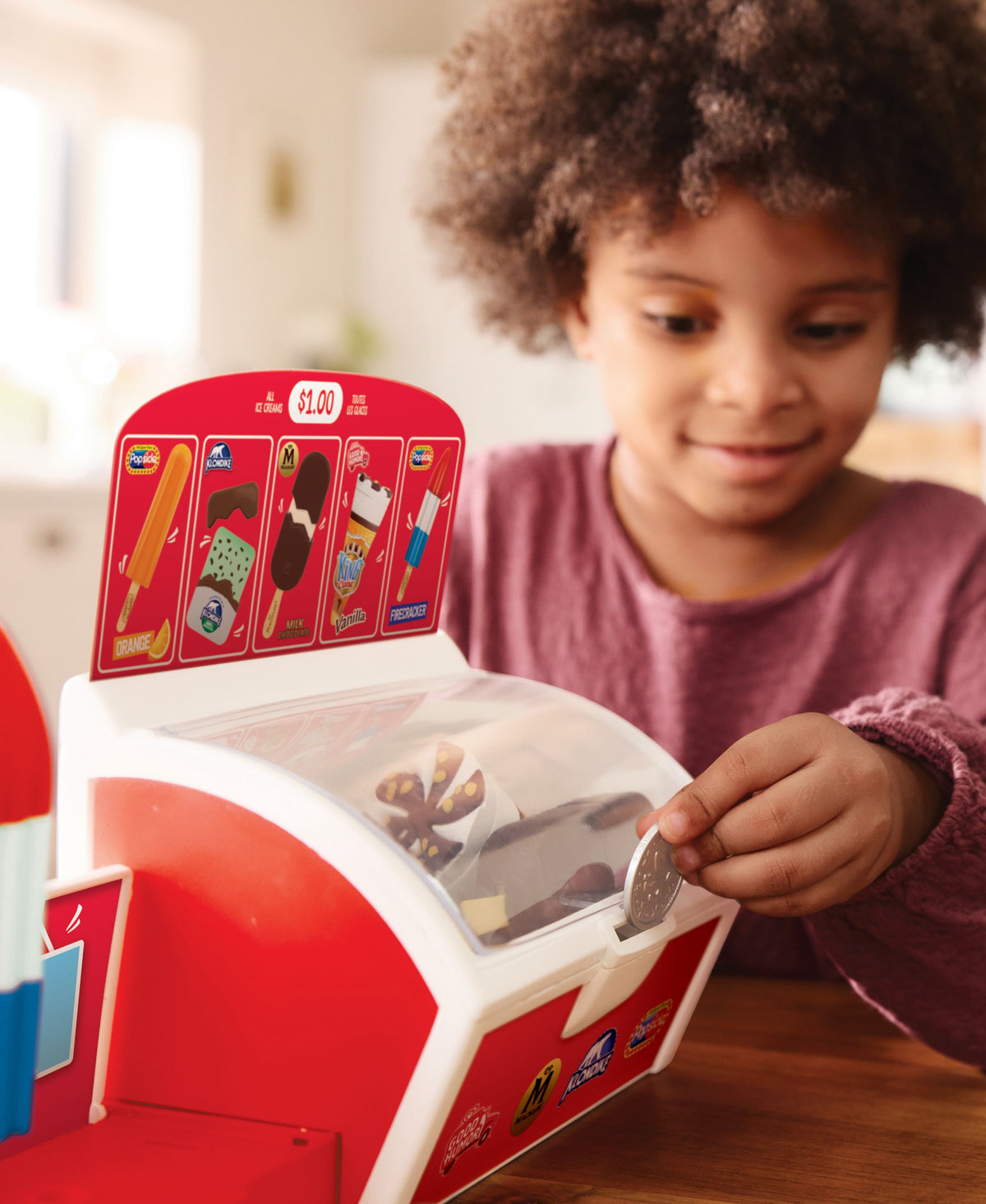 Child playing with red Casdon Ice Cream Shop playset, inserting coin into freezer dispenser
