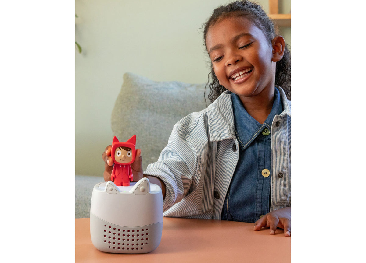 Girl smiling at white Toniebox Lite speaker with red Rubie Creative Tonie character on top