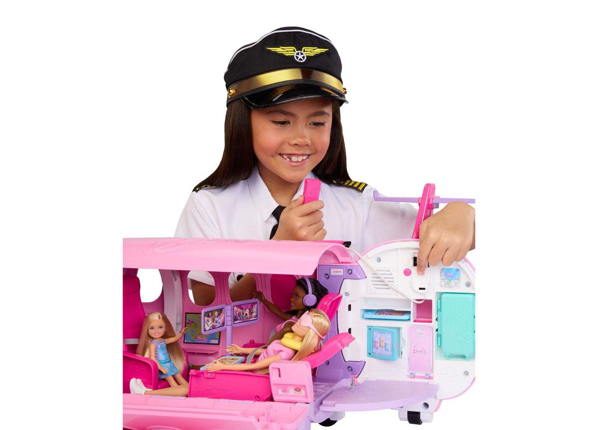 Girl in pilot uniform playing with pink Barbie Dream Plane playset featuring airplane cabin interior, dolls, and acce...