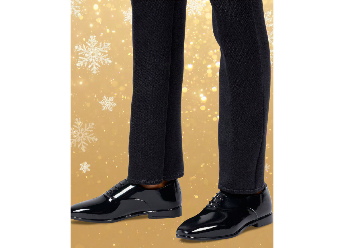 Barbie 2026 Holiday Ken doll wearing black tuxedo with polished shoes against gold snowflake background