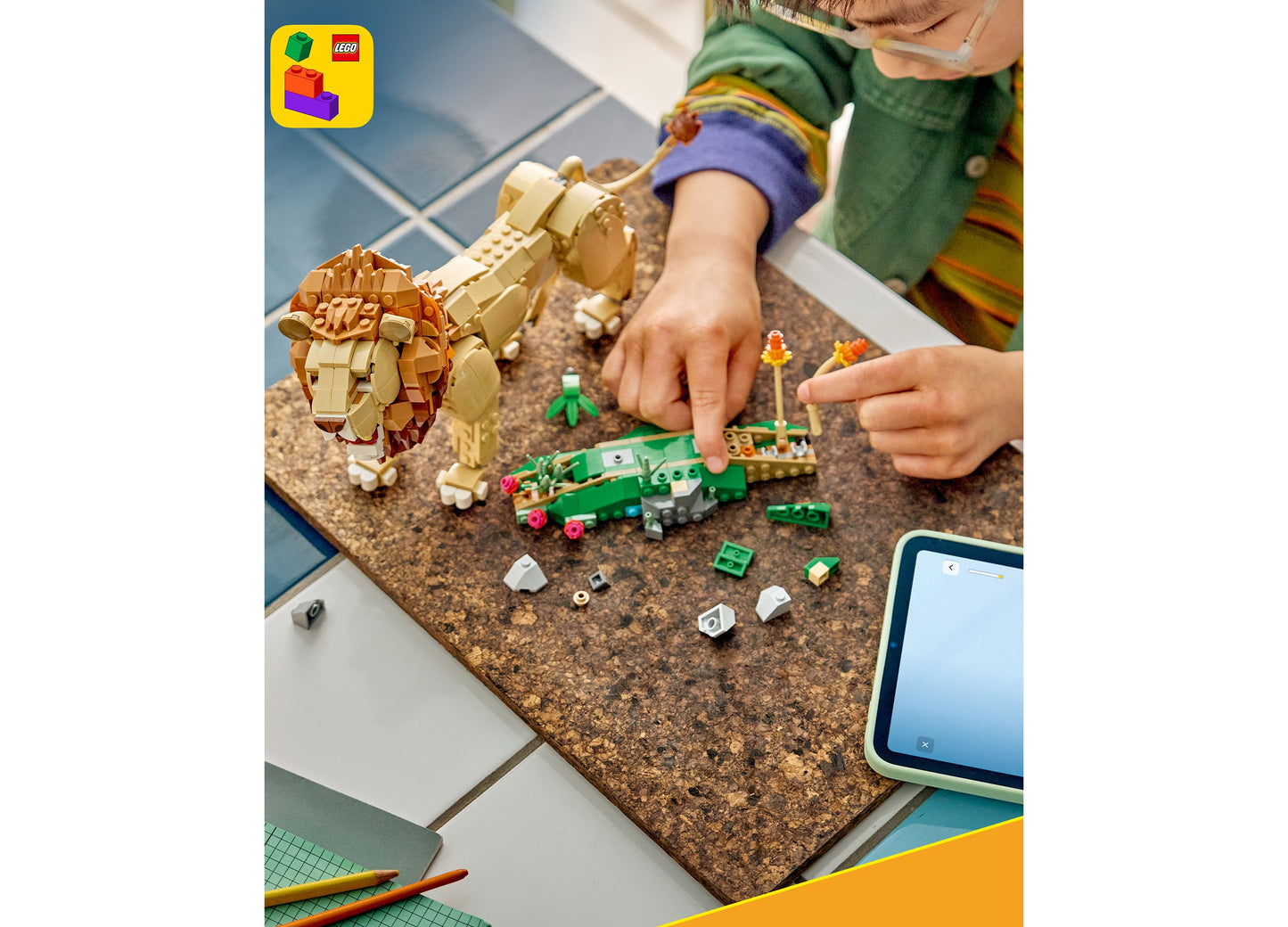 Child building LEGO Wild Animals Majestic Lion 31386 set with tan lion and green accessories on cork mat