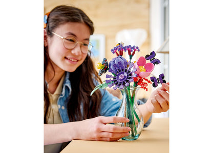 Girl with glasses smiling at colorful LEGO Flower Bouquet building set in glass vase with purple, pink, and red flowers
