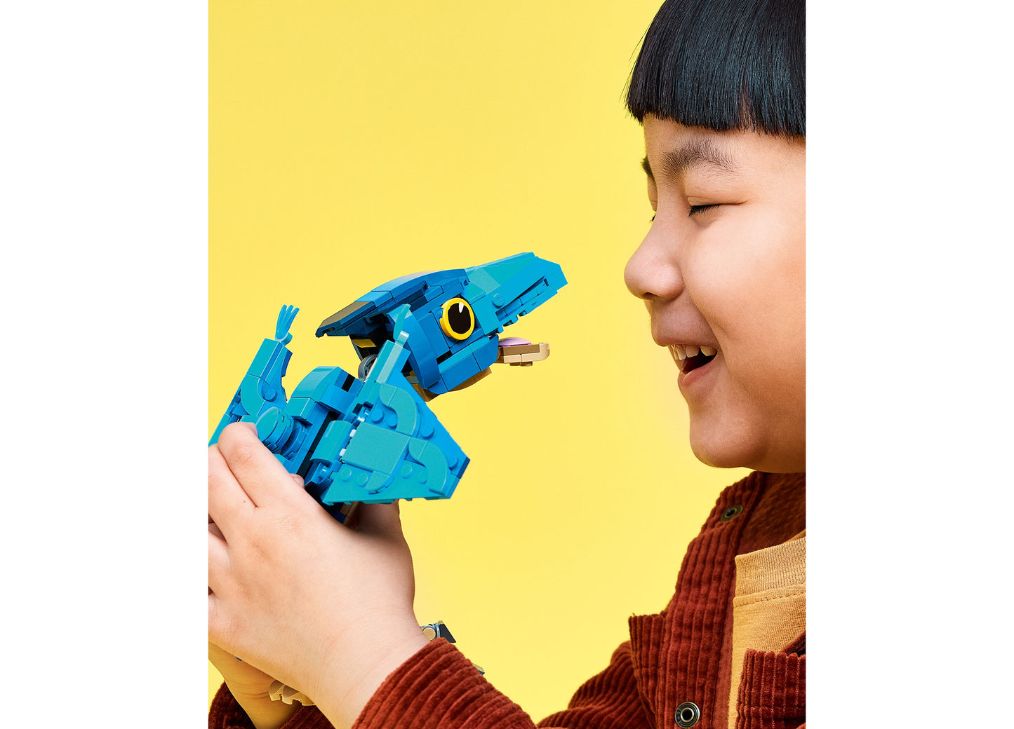 Child holding blue LEGO Jurassic World Pteranodon dinosaur toy set against yellow background