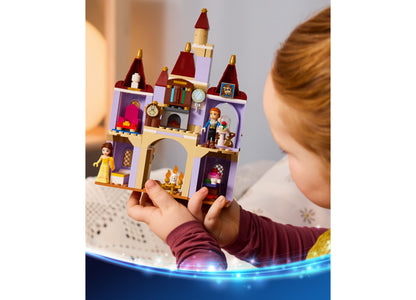 Child holding LEGO Disney Princess Belle's Enchanted Castle set with purple towers, red roofs, and minifigures