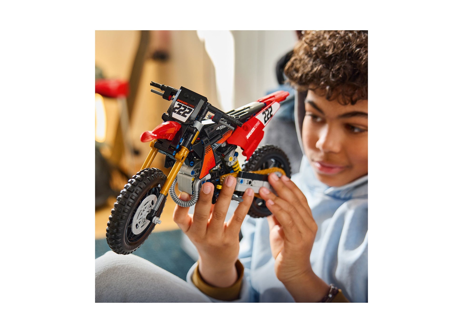 Child holding red LEGO Ducati Desmo450 MX motorcycle building set with black and gold details