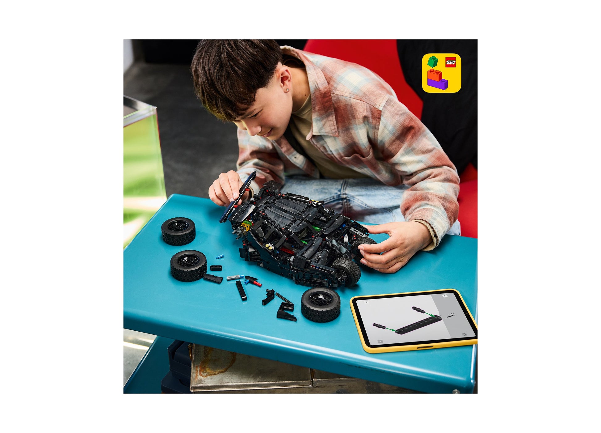 Child assembling LEGO Batman Batmobile Tumbler 42239 remote-control set on blue table with instruction manual
