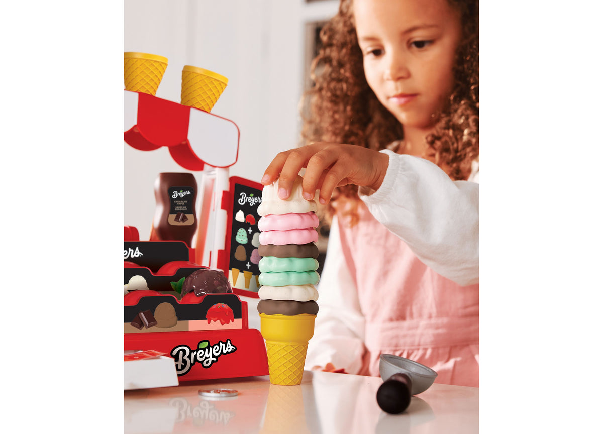 Child stacking colorful Breyers ice cream cone pieces in yellow cone from Casdon Ice Cream Parlor playset