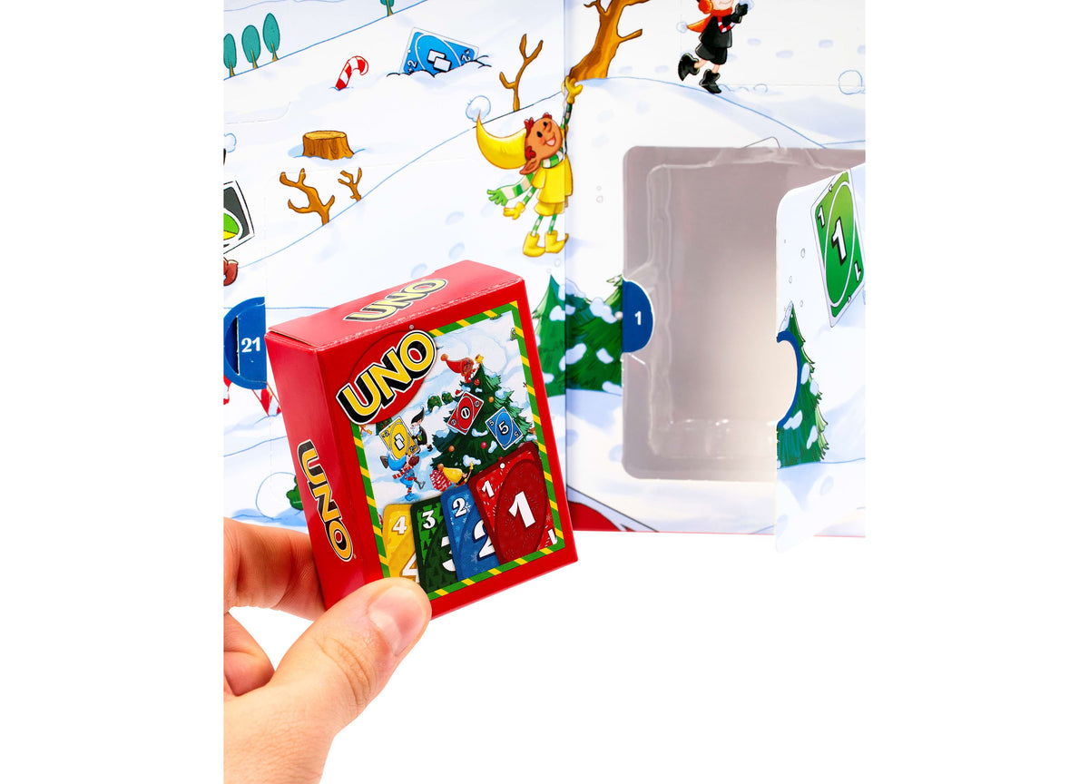 UNO Advent Calendar with red box featuring numbered doors 1-24, held in hand against snowy winter scene backdrop