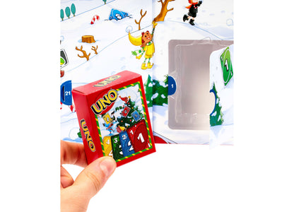 UNO Advent Calendar with red box featuring numbered doors 1-24, held in hand against snowy winter scene backdrop