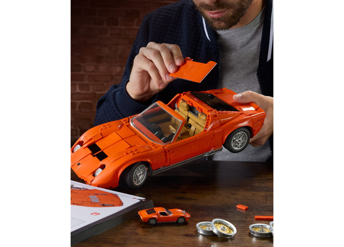 Man holding orange Lamborghini Miura P400 SV building set with opening doors and hood, displayed with instruction man...