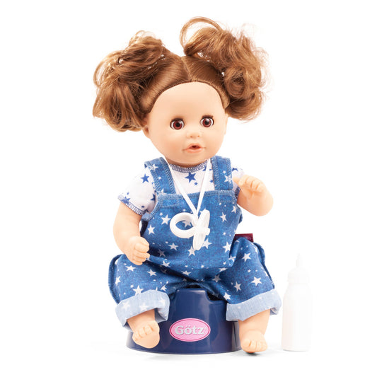 Gotz Aquini baby doll with brown curly hair in pigtails, wearing blue star-print overalls and white star-print shirt, seated on navy potty trainer with pink Got