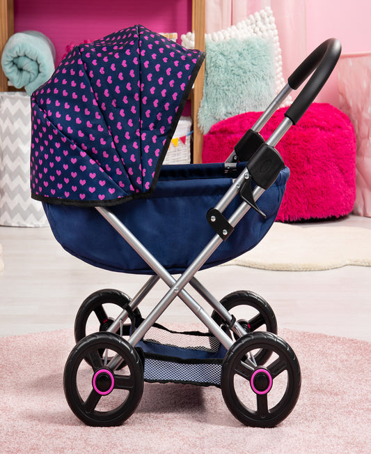 Doll pram stroller with navy blue frame, pink heart-patterned canopy, black wheels with pink accents, displayed in styled room setting with plush pillows and bl