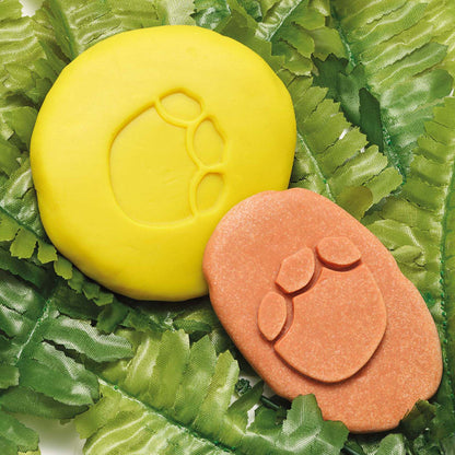 Dinosaur Footprint Fossils Discovery Set with yellow and terracotta fossil molds on green leaf background