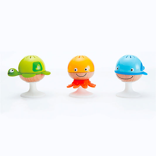 Three colorful suction-cup rattles with smiling faces: green turtle, yellow octopus, and blue whale, each with a wooden ball body and white suction-cup base