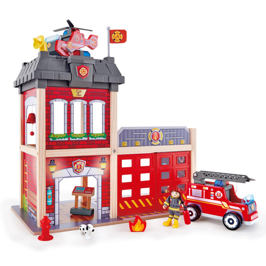 Hape City Fire Station wooden playset with red brick building, helicopter on roof, fire truck, firefighter figure, dalmatian dog, fire hydrant, and flame access