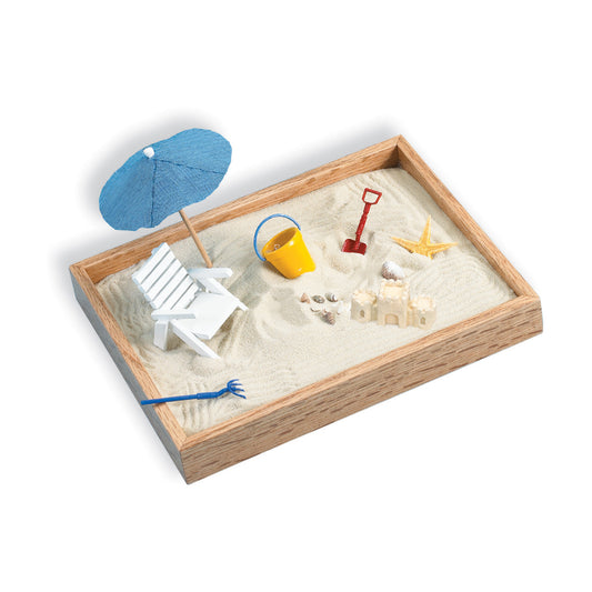Wooden sandbox filled with sand containing beach-themed miniature accessories including blue umbrella, white beach chair, yellow bucket, red shovel, starfish, s