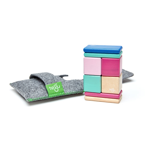 Tegu magnetic wooden blocks in blue, mint, pink, hot pink, and natural wood, stacked and displayed next to gray felt storage pouch with green Tegu label
