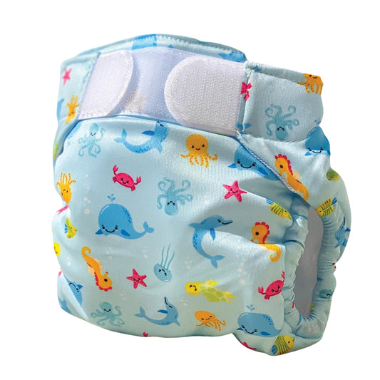 Light blue swim nappy with colorful sea creatures including whales, seahorses, jellyfish, starfish, and fish; white absorbent panel visible at top