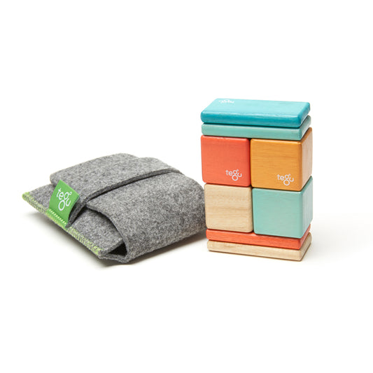 Tegu magnetic wooden blocks in turquoise, green, orange, yellow, and natural wood, stacked in a tower next to a gray felt storage pouch with green trim