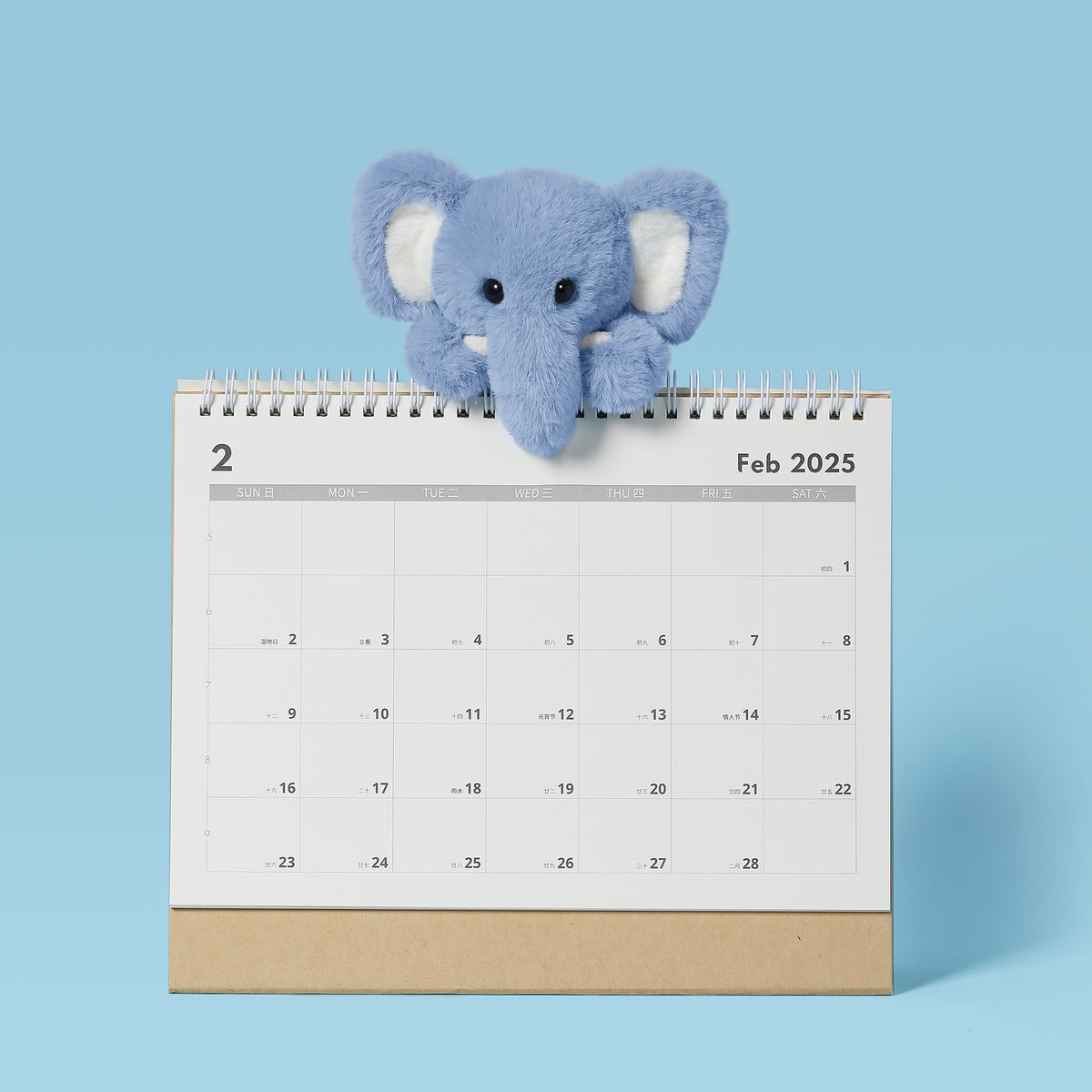 Lazy Series Mini Comfort Elephant 6-inch plush in lavender blue with white inner ears, sitting on February 2025 calendar