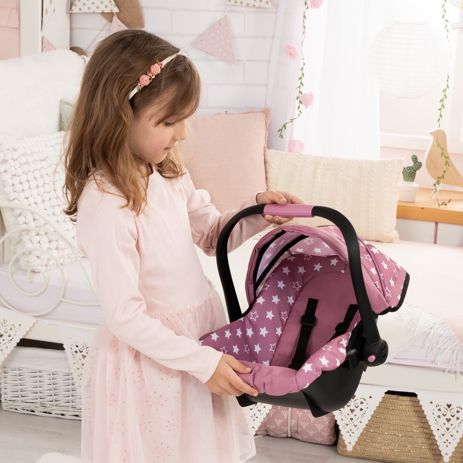 Bayer Design Deluxe Car Seat in pink with white stars pattern, held by child