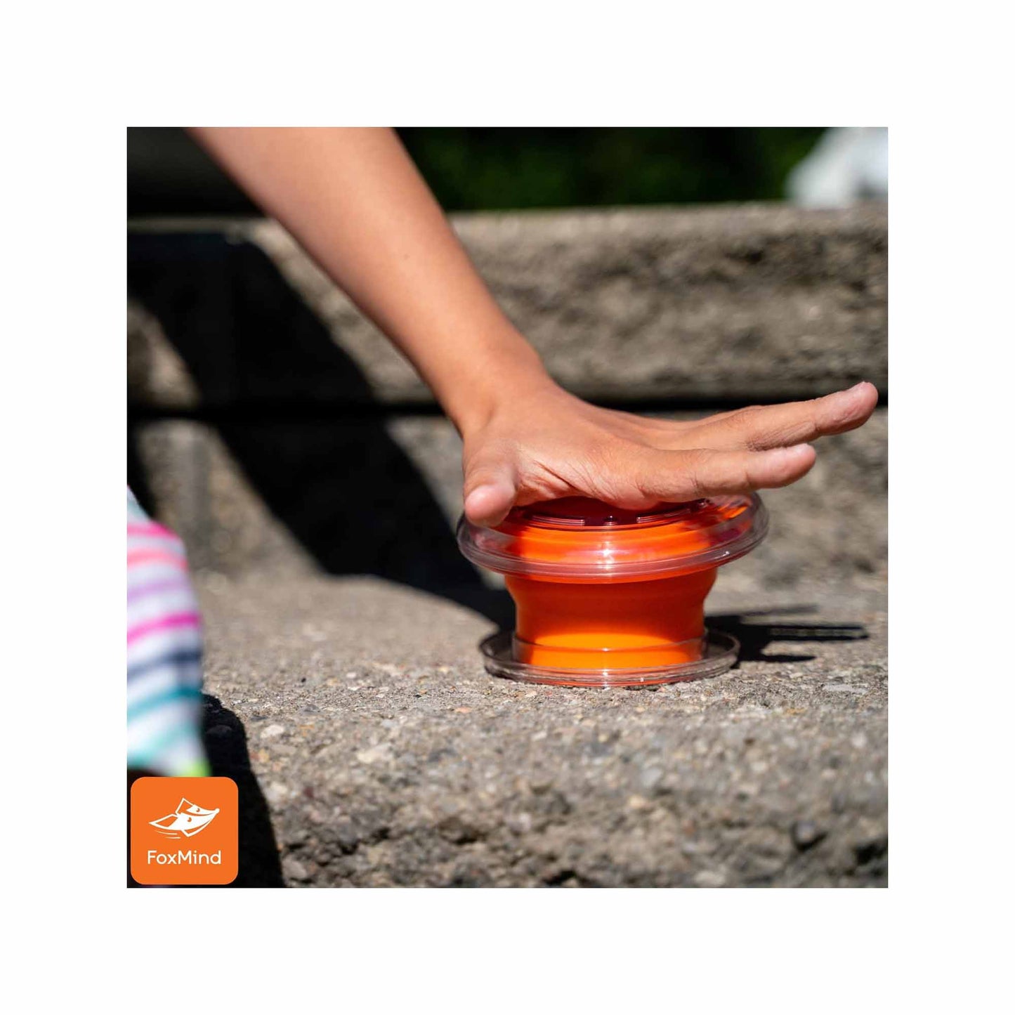 Foxmind Slam Bluff interactive game with orange dome toy being touched by child's hand on pavement