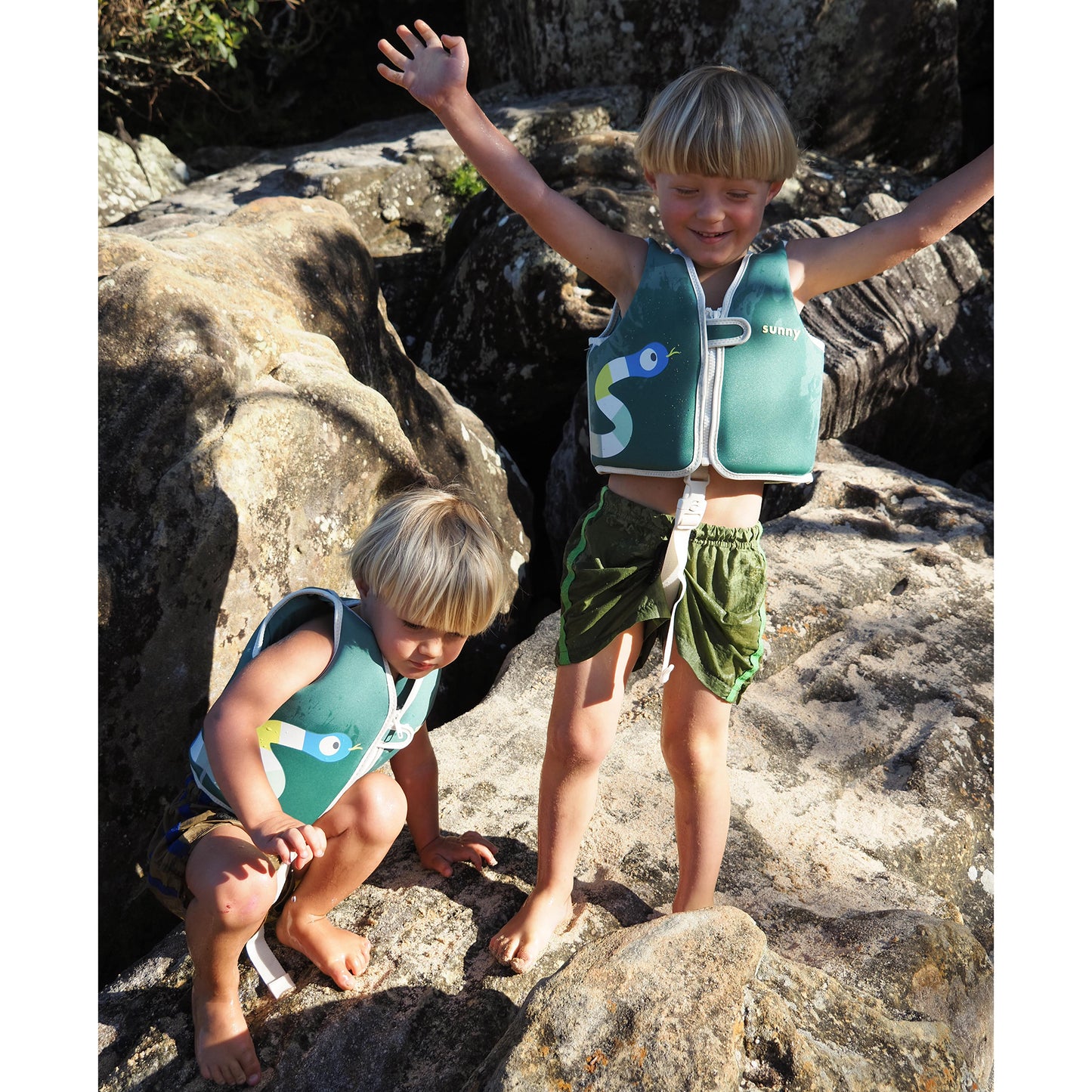 Sunnylife Into The Jungle Float Vest in green with fish design, worn by child at beach