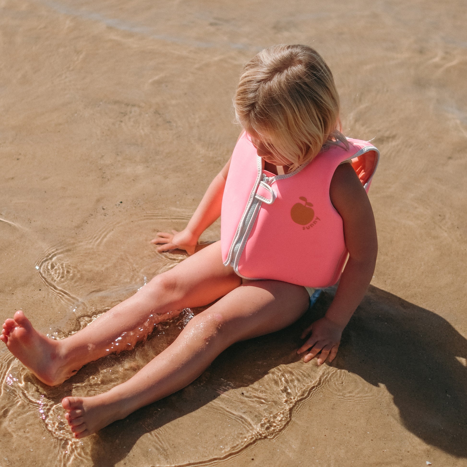 Neon pink Float Vest for toddlers, worn by child in shallow water at beach