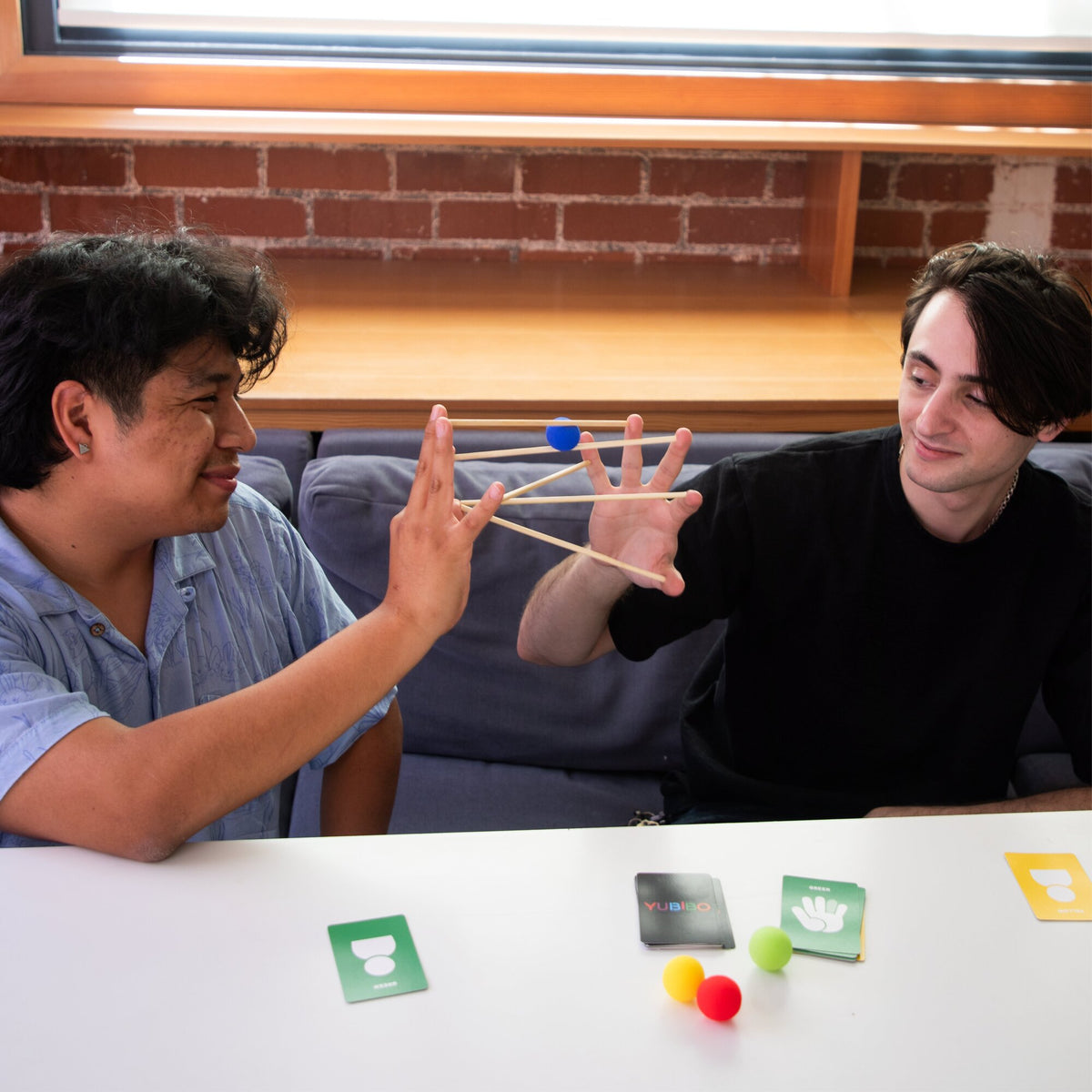 KESS Yubibo cooperative party game with wooden sticks and colorful balls, two players demonstrating hand coordination...