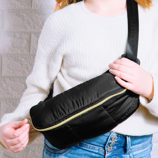 Black puffer crossbody bag with gold zipper, modeled by a child wearing white sweater and blue jeans