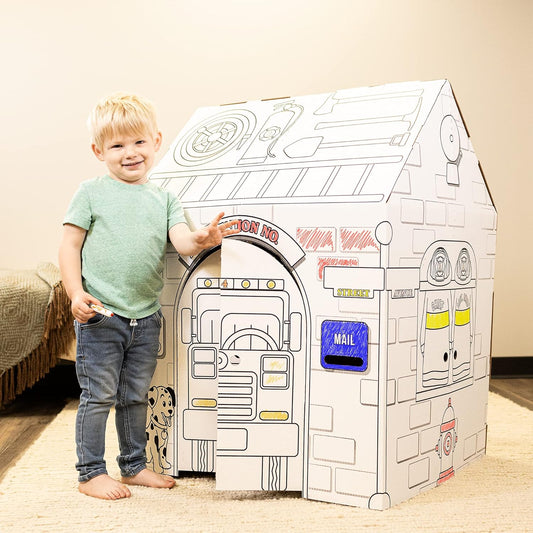 Toddler on model with cardboard playhouse featuring police car and fire truck designs, interactive elements including steering wheel and mail slot