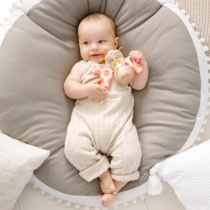 Butterfly Rainmaker Robert toy in baby's hands, soft beige and coral colors