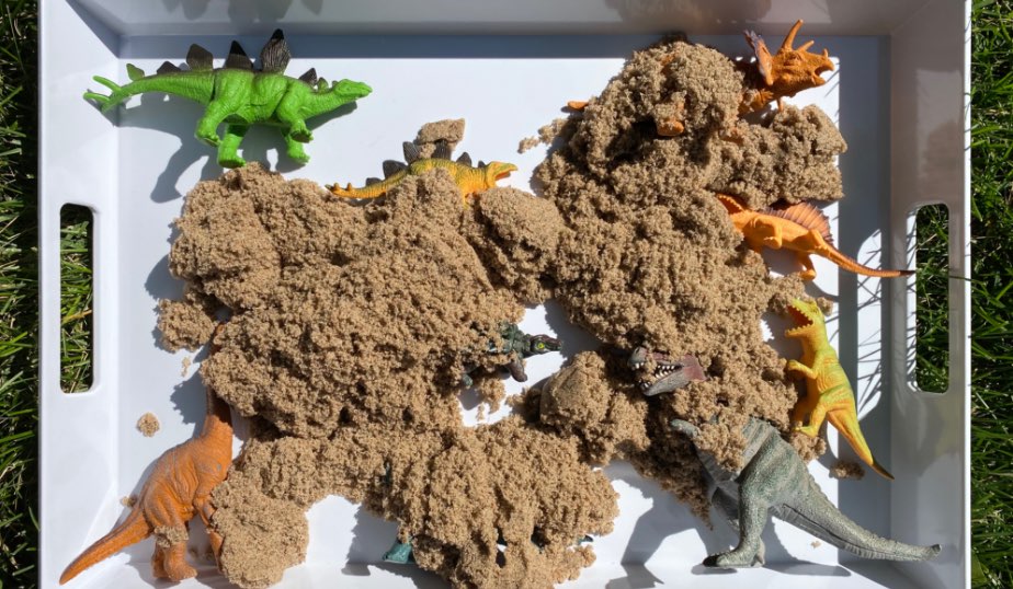 dinosaur figures covered in kinetic sand for dino discovery box diy for kids